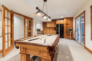 Une table de billard dans une pièce dotée de meubles en bois, d’un réfrigérateur et d ’une porte à panneaux de verre.