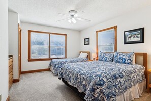 A bedroom with two beds, a ceiling fan, and large windows with blinds. - Ocean Paradise -- Spacious 7BR Oceanfront with Pool, Hot Tub and More! (Corolla)
