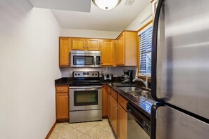 A compact kitchen with wooden cabinets, a stainless steel refrigerator, a microwave, an oven, a dishwasher, and a coffee maker. - Keepers Loft -- Waterfront Duplex with Pier and Gazebo (Duck)