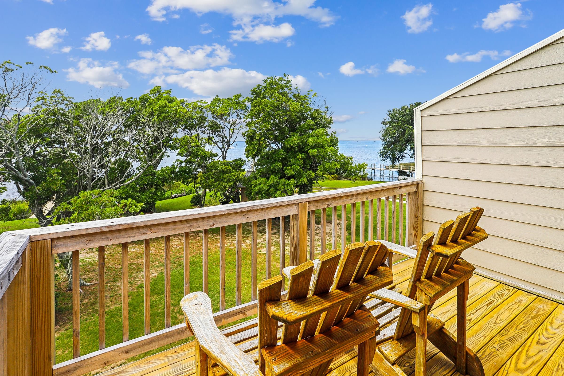 A wooden deck with a view of a lake and trees, and a building with beige siding.