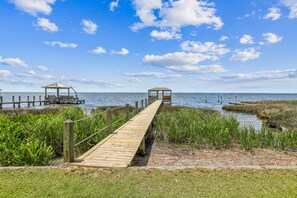 A wooden boardwalk leading to two gazebos over water, surrounded by grassy areas.
