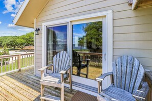 A wooden deck with two Adirondack chairs and a glass door leading to a patio area. - Emerald Duck -- Awesome Sunset and Water Views Soundfront Duplex (Duck)