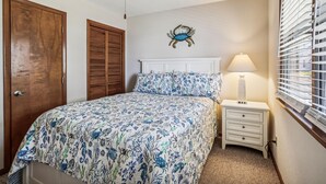 A bedroom with a bed, a nightstand, a lamp, a ceiling fan, a wooden door, and a wall-mounted crab decoration. - Emerald Duck -- Awesome Sunset and Water Views Soundfront Duplex (Duck)