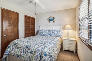 A bedroom with a bed, a nightstand, a lamp, a ceiling fan, a wooden door, and a wall-mounted crab decoration. - Emerald Duck -- Awesome Sunset and Water Views Soundfront Duplex (Duck)