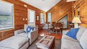 A cozy living room with wooden walls, a ceiling fan, and a dining area with wicker furniture. - Emerald Duck -- Awesome Sunset and Water Views Soundfront Duplex (Duck)