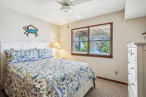 Un dormitorio con cama, ventilador de techo, ventana con persianas y una lámpara de pared.