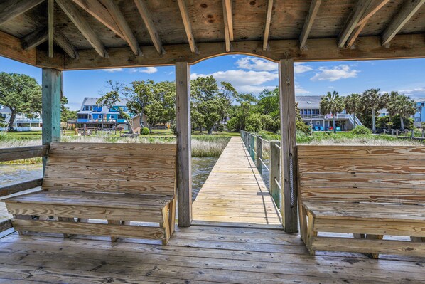 Una terraza de madera con bancos, vista despejada a la playa y casas al fondo.