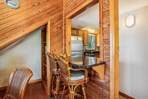 A wooden interior with a dining area featuring wicker chairs and a kitchen with wooden cabinets and a refrigerator.
