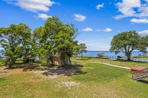 A park with trees, a small shed, a dock, and a body of water in the background.