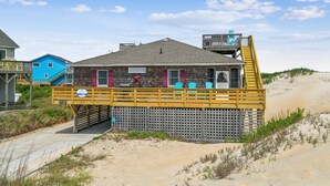 A beach house with a wooden deck, a small upper deck, and a staircase leading to the upper deck.
