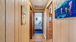 A wooden hallway with a bed in the background, a painting on the wall, and a sign with a quote.