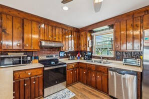 Una cocina con gabinetes de madera, estufa de acero inoxidable, microondas, tostadora y lavavajillas.