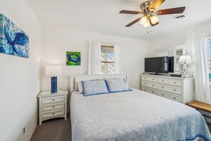 Une chambre à coucher comprenant un lit, une table de chevet, une commode, un téléviseur et un ventilateur de plafond.