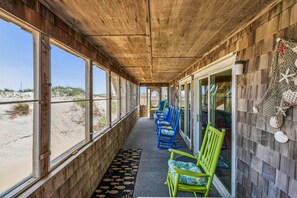 A covered outdoor seating area with wooden walls, large windows, and beach views.