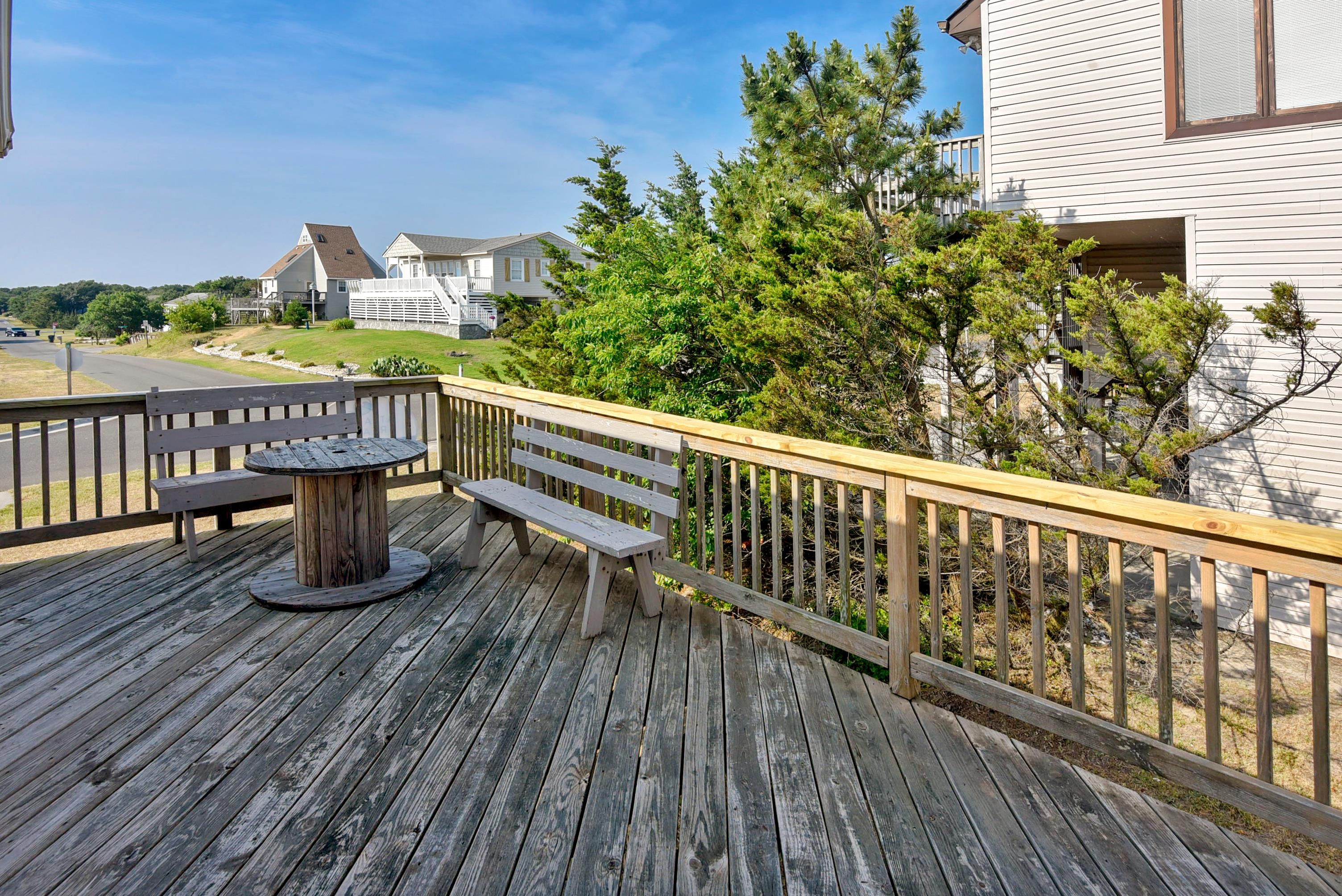 A wooden deck with a round table and benches, overlooking a residential area with houses and trees.
