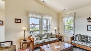 A living room with a sofa, a coffee table, and two lamps. There are windows with curtains and a view of the outside. - Premium Tripp -- Close to Shopping, Restaurants and Activities (Kill Devil Hills)