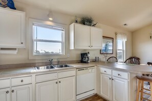 A kitchen with white cabinets, a double sink, a coffee maker, and a dining area with wooden chairs. - Premium Tripp -- Close to Shopping, Restaurants and Activities (Kill Devil Hills)