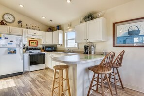A kitchen with white cabinets, a stove, a microwave, and a sink. There are two wooden stools and a small island with a sink. - Premium Tripp -- Close to Shopping, Restaurants and Activities (Kill Devil Hills)