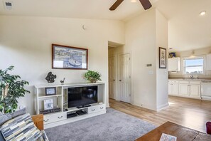 A living room with a flat-screen TV, a coffee table, and a sofa. There is a hallway leading to a kitchen with white cabinets and a window. - Premium Tripp -- Close to Shopping, Restaurants and Activities (Kill Devil Hills)