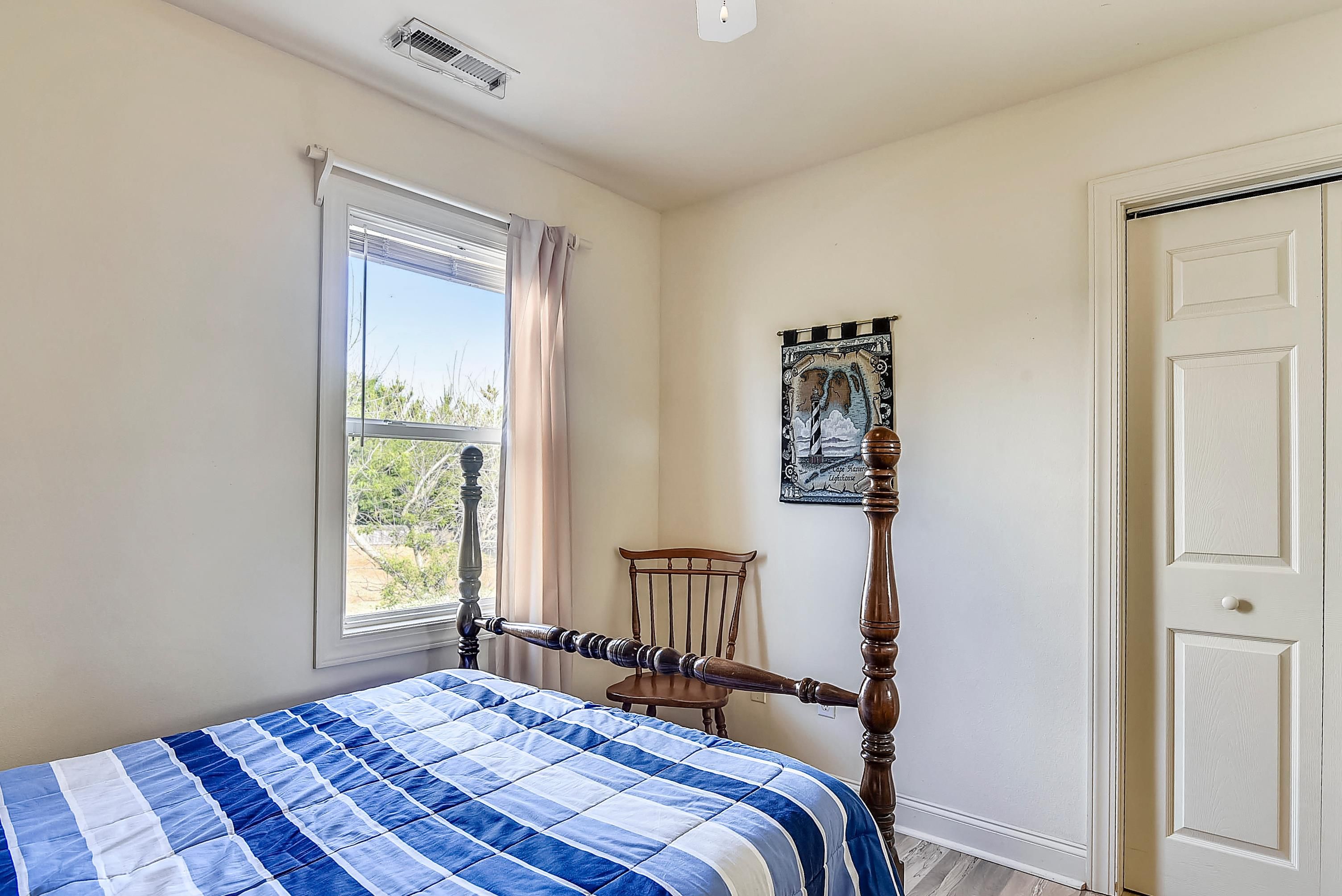A bedroom with a bed, a window with curtains, a chair, a door, and a wall-mounted picture.