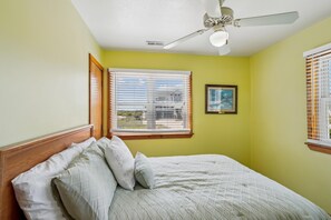 A bedroom with a bed, a ceiling fan, a window with blinds, and a framed picture on the wall.