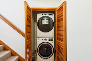 A laundry room with a top-loading washer and a front-loading dryer, wooden slats on the walls, and a carpeted staircase.