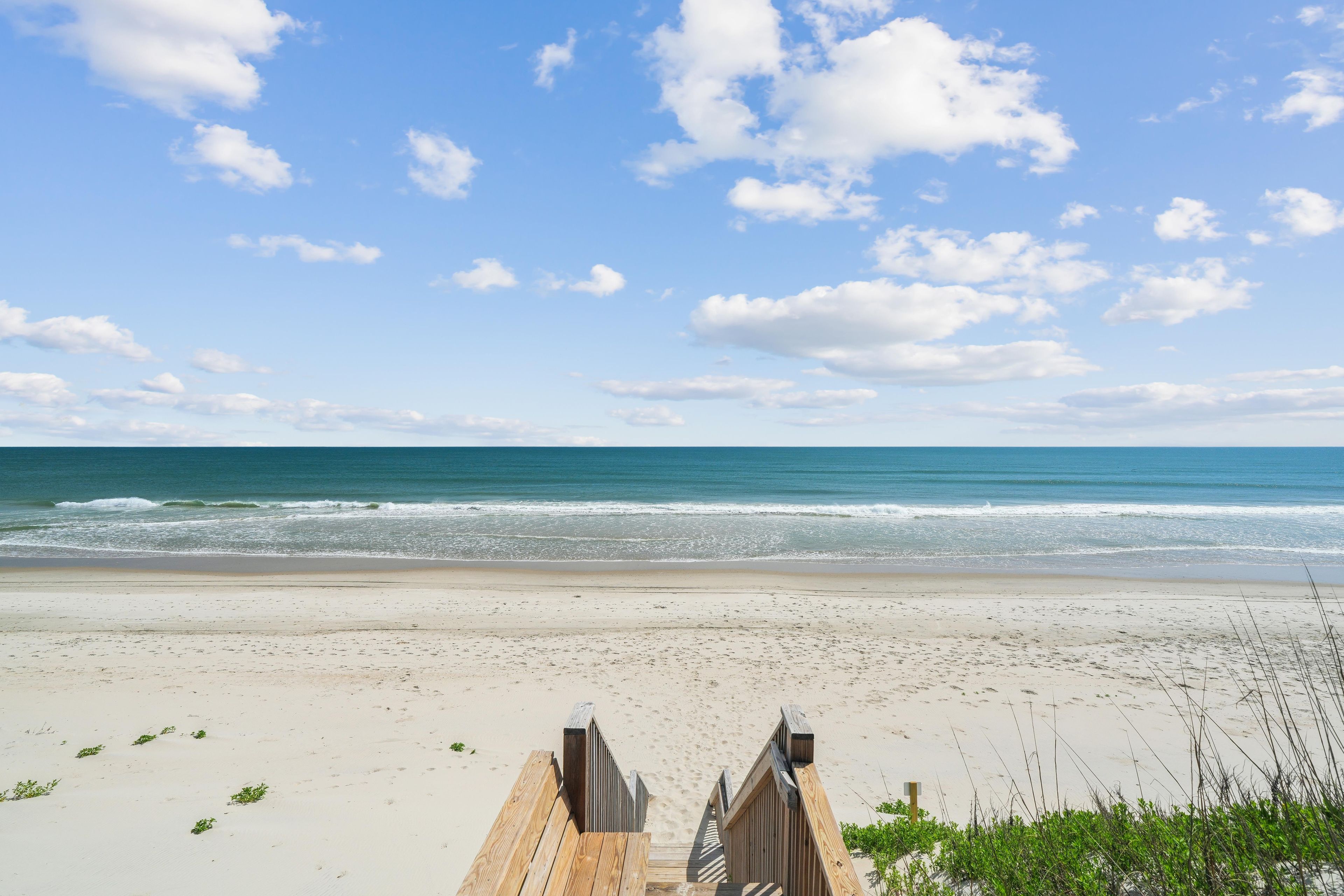 Une plage avec une promenade en bois menant à l’eau, une plage de sable et un ciel dégagé.