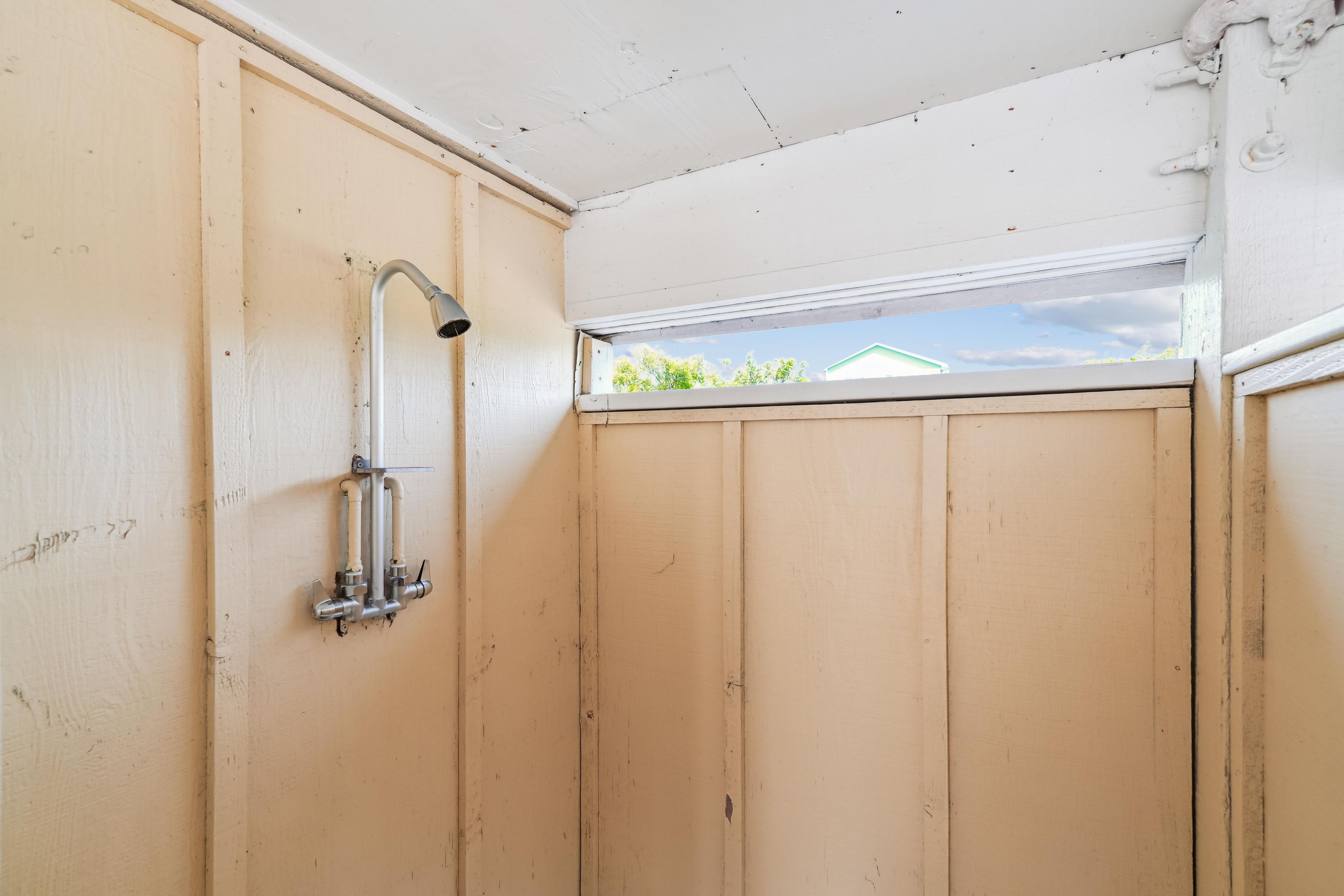 A small, enclosed space with a shower, a window, and a view of greenery outside.