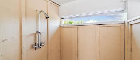 A small, enclosed space with a shower, a window, and a view of greenery outside.