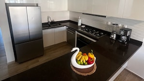 Uma cozinha moderna com armários brancos, uma geladeira de aço inoxidável, um fogão a gás e uma cafeteira.