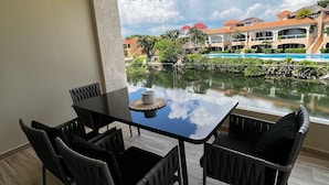 Uma sala de jantar com mesa e cadeiras, vista para uma piscina e edifícios ao fundo.