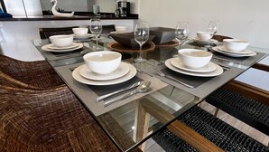 Uma sala de jantar moderna com uma mesa de vidro posta para quatro pessoas, rodeada por cadeiras de vime.