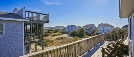 A wooden deck with a railing, overlooking a residential area with houses and a clear sky.