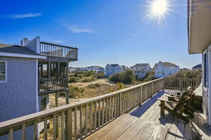 Une terrasse en bois avec une rambarde, donnant sur un quartier résidentiel avec des maisons et un ciel dégagé.