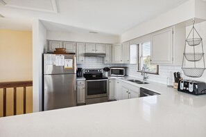 Una cocina moderna con electrodomésticos de acero inoxidable, muebles de color blanco y un organizador de cocina colgante.