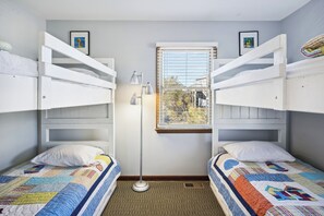 A room with two bunk beds, a window with blinds, a floor lamp, and a quilt on the beds.