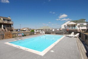 A rectangular swimming pool with a wooden deck surrounding it, a lifeguard stand, and a wooden fence.