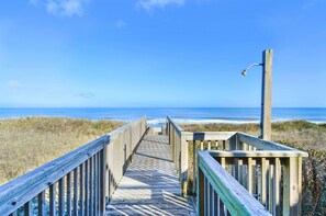 A wooden boardwalk leading to the beach with a wooden railing on one side and a street lamp on the other.