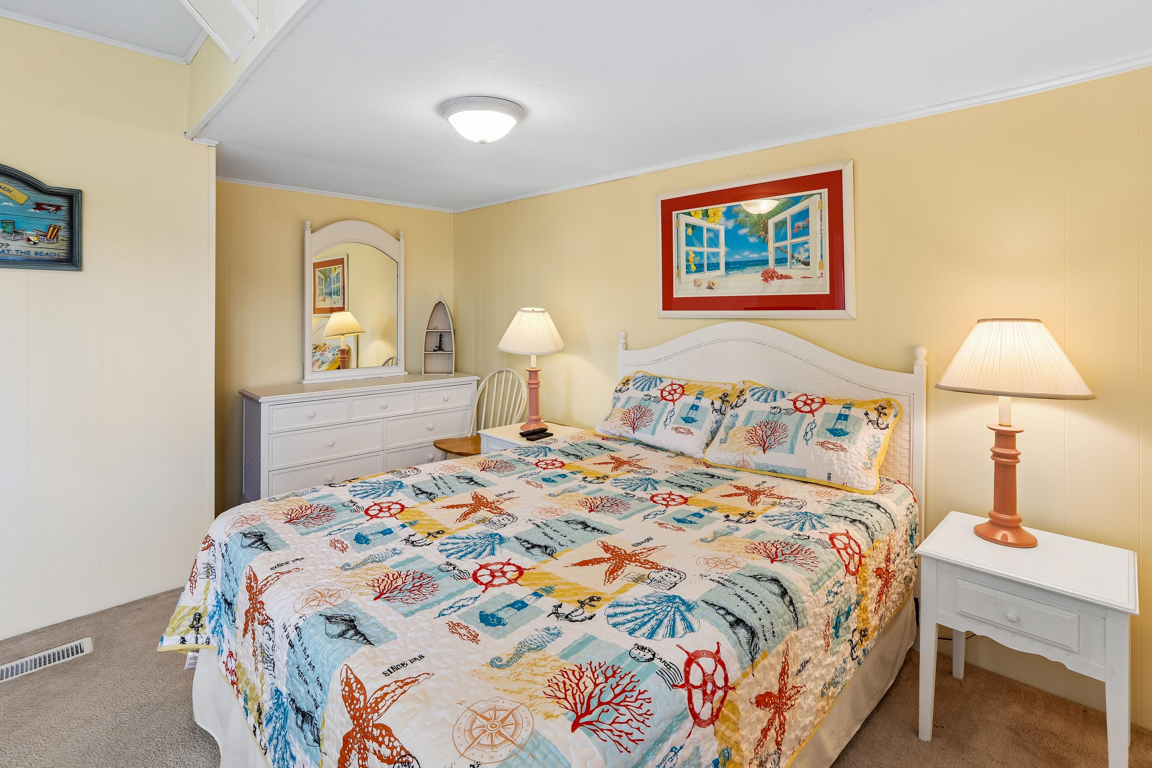 Une chambre à coucher comprenant un lit, des tables de chevet, une commode, un miroir et des œuvres d’art murales.