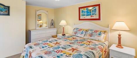 Une chambre à coucher comprenant un lit, des tables de chevet, une commode, un miroir et des œuvres d’art murales.