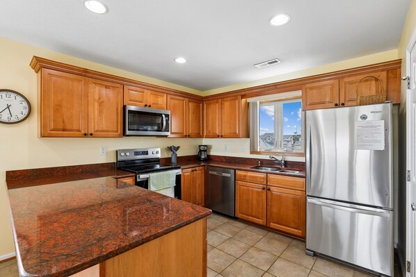 A kitchen with wooden cabinets, stainless steel appliances, a granite countertop, and a window with a view.