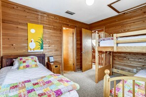 A wooden cabin-style room with a bunk bed, a single bed with a colorful quilt, a nightstand, and a painting on the wall. - Timberland -- 4 BR Oceanside home in Southern Duck (Duck)