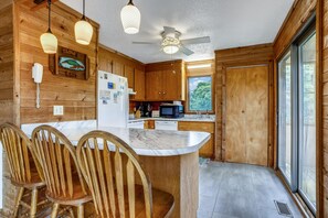 A wooden cabin interior with a kitchen, dining area, and a large window.