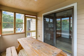 Une pièce avec une table et un banc en bois, une porte-fenêtre coulissante et des fenêtres donnant sur un paysage verdoyant.