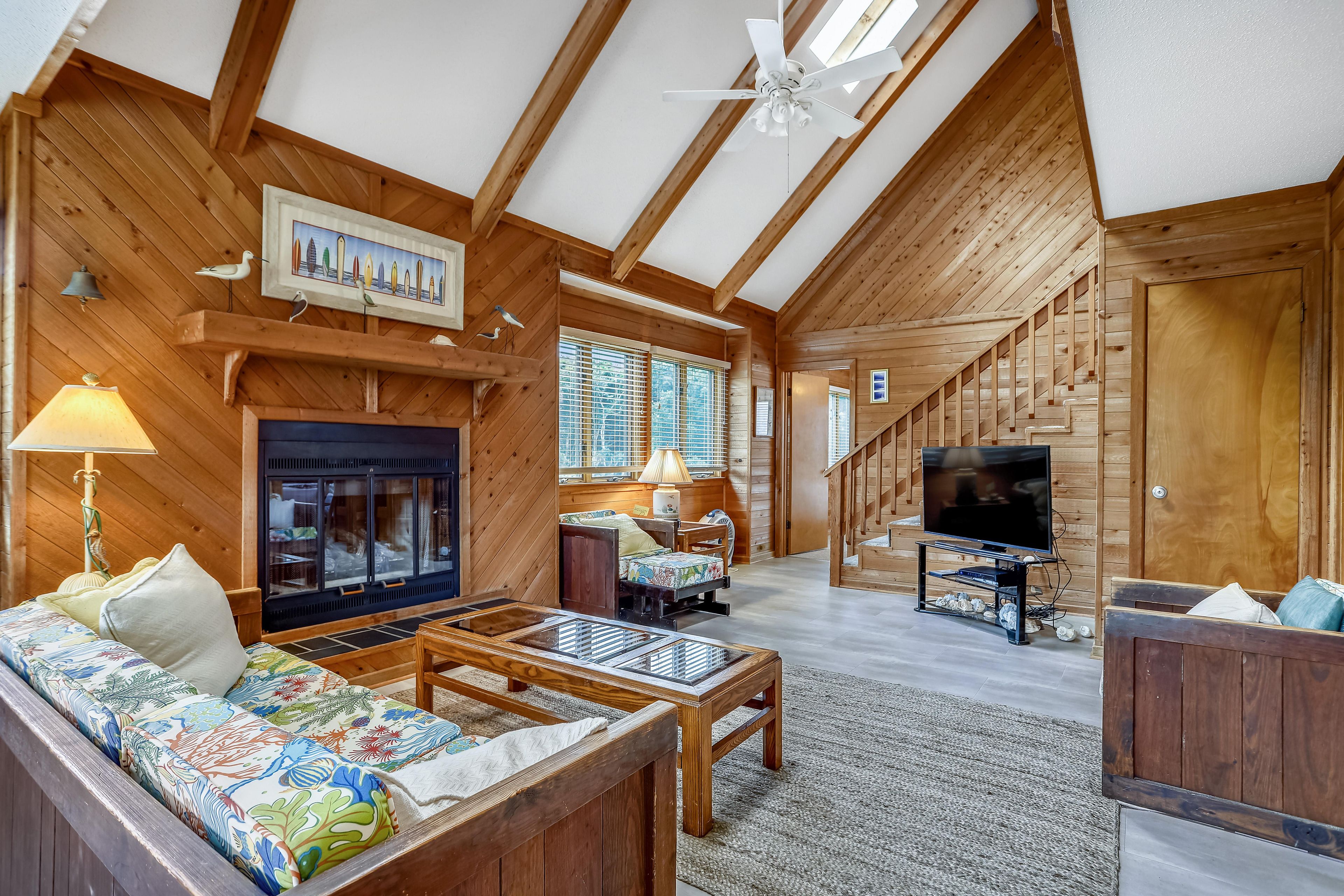 A log cabin interior with a fireplace, sofa, television, and wooden ceiling beams.
