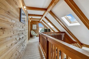 Un intérieur en bois avec un plafond en pente, une chaise et une vue à travers un puits de lumière.