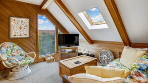 A cozy attic room with a sloped ceiling, a framed marine life illustration, a television, and a small table with a fan. - Timberland -- 4 BR Oceanside home in Southern Duck (Duck)