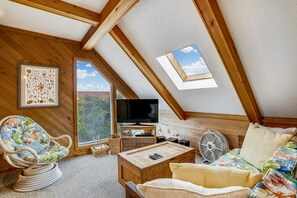Une pièce mansardée chaleureuse avec un plafond en pente, une illustration encadrée représentant la vie marine, un téléviseur et une petite table avec un ventilateur.