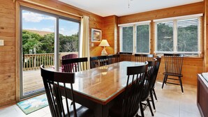 A wooden interior with a dining table, chairs, a ceiling fan, and large windows.