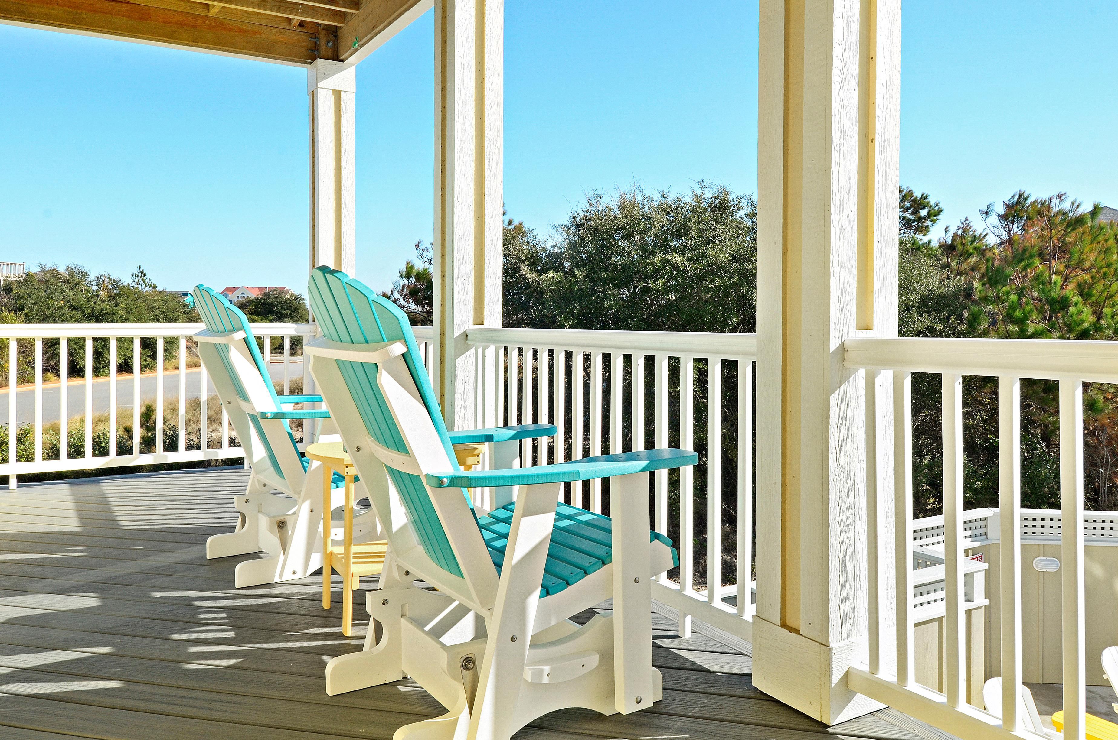 A wooden deck with two Adirondack chairs and a white railing.